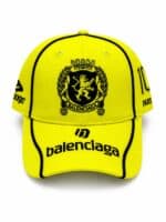 Bright yellow Balenciaga baseball cap featuring a black crest emblem, with 'balenciaga' text on the brim and 'PARIS' on the side.