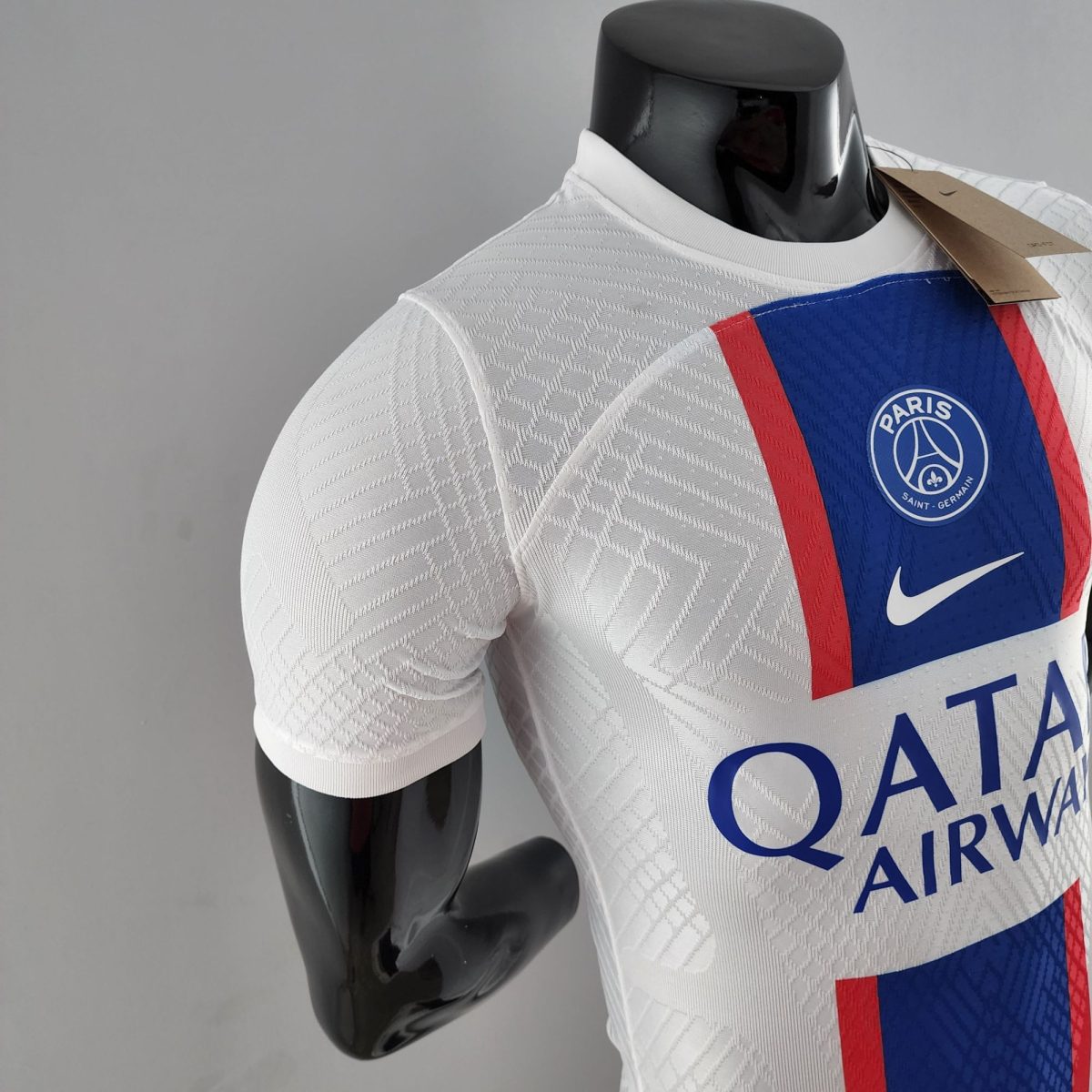 Black mannequin wearing a white Paris Saint-Germain jersey with a blue and red stripe and a hanging tagglossed on the chest area.