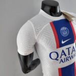 Black mannequin wearing a white Paris Saint-Germain jersey with a blue and red stripe and a hanging tagglossed on the chest area.