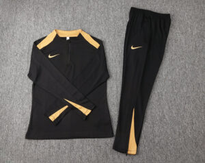 Black Nike training top with gold shoulder panels and matching black pants with a gold swoosh and inner-leg stripe.