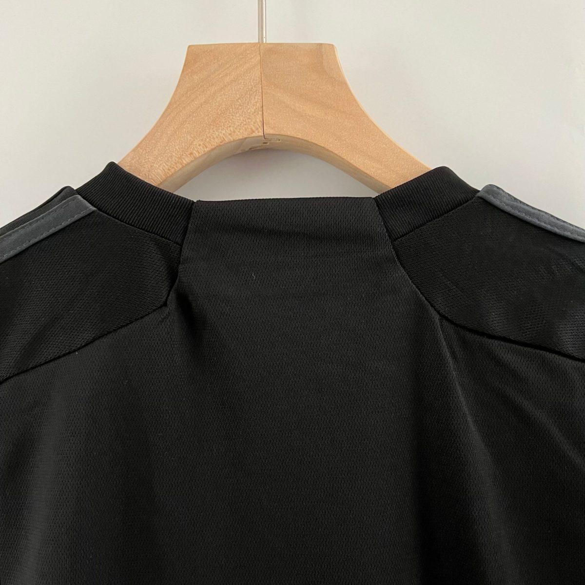 Close-up of a black polo shirt on a light wooden hanger against a pale wall, showing the collar and upper back.