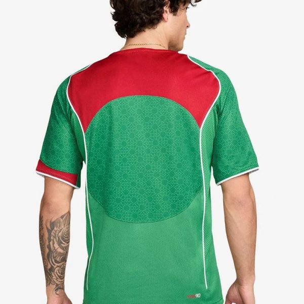 Back view of a green and red sports jersey with a circular darker green pattern on the back and white piping.
