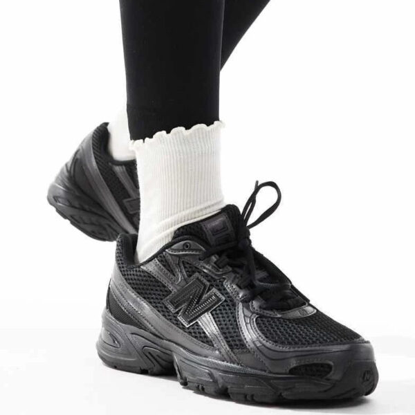 Black athletic sneaker on a person wearing white ribbed socks, with one foot raised for the pose.