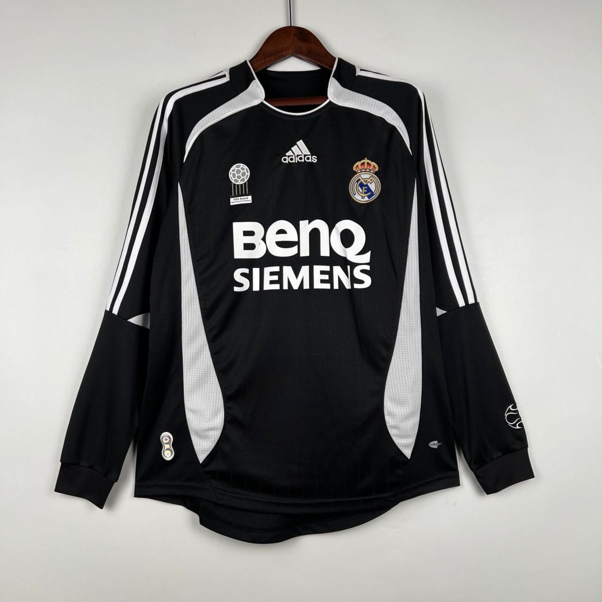 Real Madrid black soccer jersey with white piping and crest, Adidas logo, Siemens sponsor, hanging on a wooden hanger.