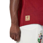 dca1c45a64a4d1700f4b3add15ba53b6 | UAE SPORT STORE Close-up of a person wearing a red shirt with a beige tag at the hem and white shorts with a crest on the leg.