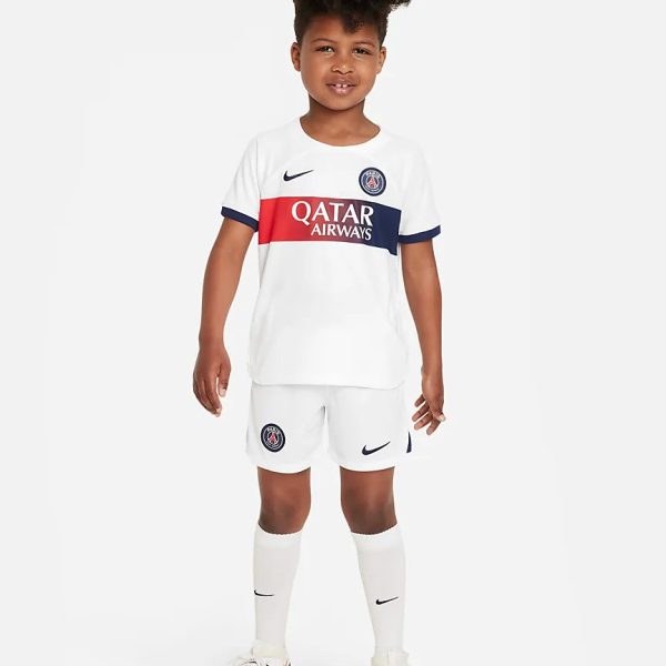 Young boy wearing a white Paris Saint-Germain home kit with Qatar Airways sponsor, standing and looking at the camera.