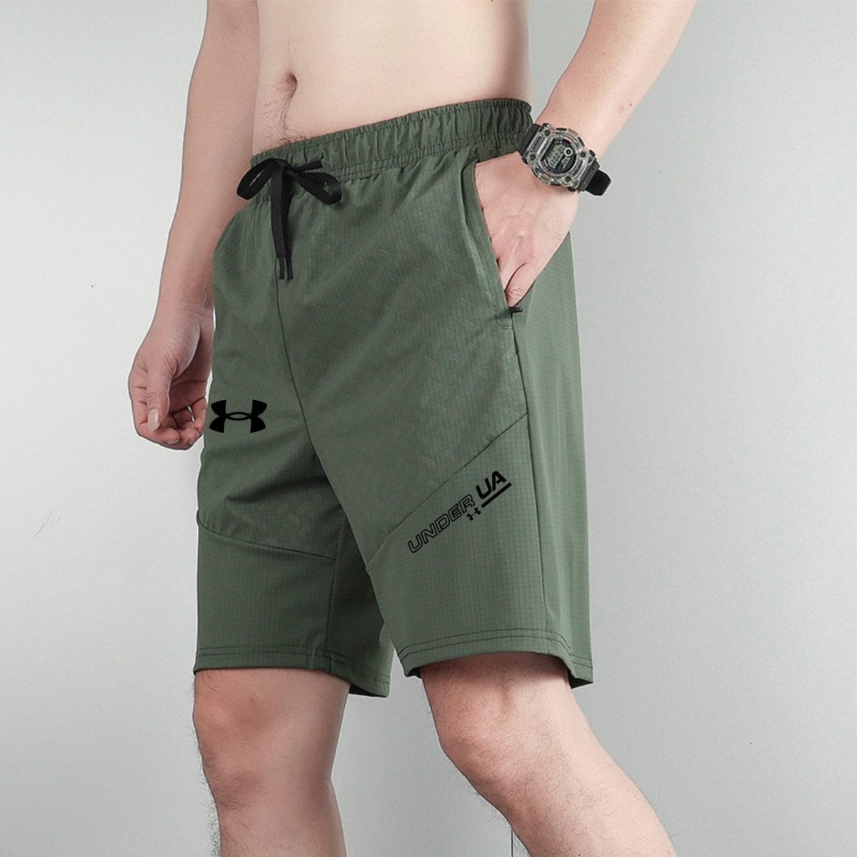 Person in olive-green athletic shorts with a black drawstring, wearing a chunky gray digital watch on the left wrist against a light background.