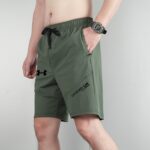 Person in olive-green athletic shorts with a black drawstring, wearing a chunky gray digital watch on the left wrist against a light background.