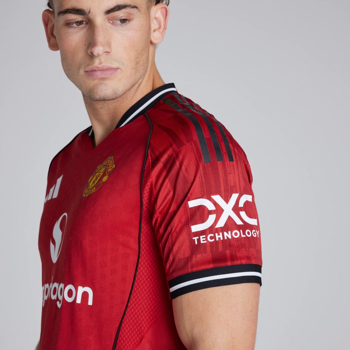 Close-up of a man wearing a red Manchester United jersey, showing the team crest on the chest and sponsor text on the sleeve (side profile).