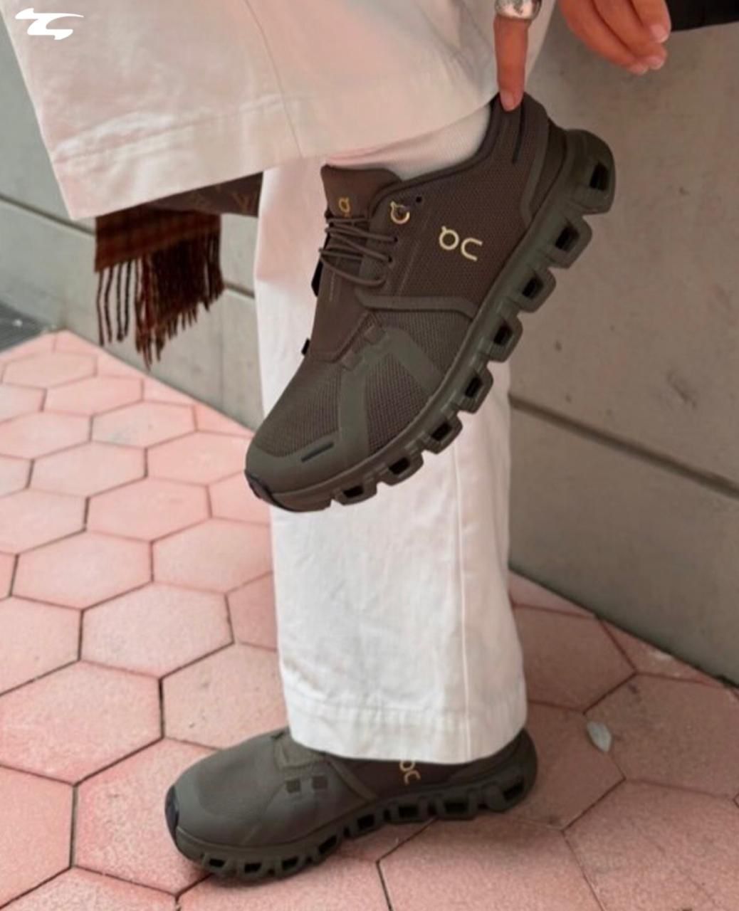 de451f20-e076-4f3a-8351-5afdce486127 | UAE SPORT STORE Olive green athletic sneaker with a chunky segmented sole, worn with white pants as the person lifts their foot.