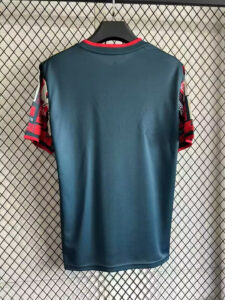 Back view of a teal polo jersey on a hanger, with red patterned sleeves, hanging against a chain-link backdrop.