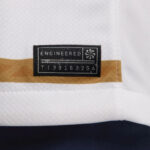 Close-up of black fabric tag reading 'ENGINEERED' with a serial line 'T1391632GA' on a white garment with a tan stripe nearby