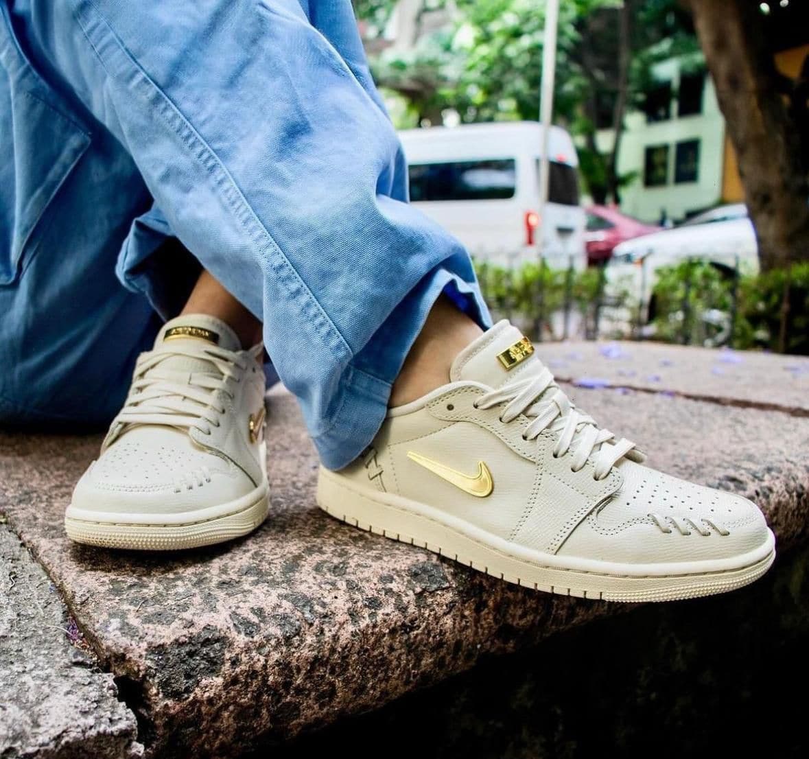 dee332e8-3964-45ac-b701-3cc4223e4692 | UAE SPORT STORE Beige Nike sneakers with a gold swoosh, worn with light blue jeans, resting on a stone curb outdoors.