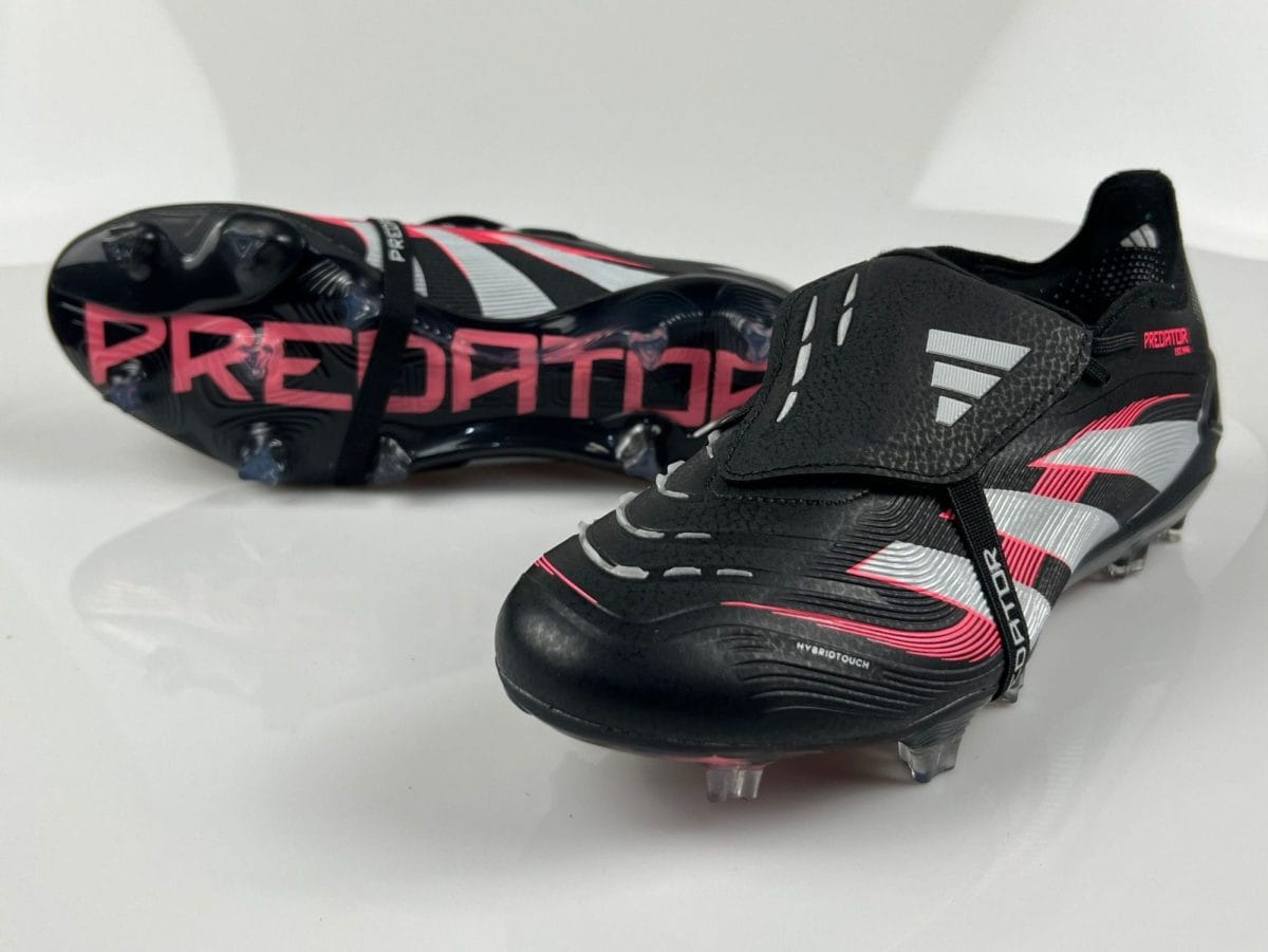 Pair of black and pink Adidas Predator soccer cleats with silver accents, shown on a white surface, highlighting studded soles and side branding.