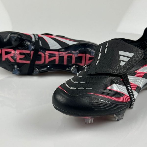 Pair of black and pink Adidas Predator soccer cleats with silver accents, shown on a white surface, highlighting studded soles and side branding.