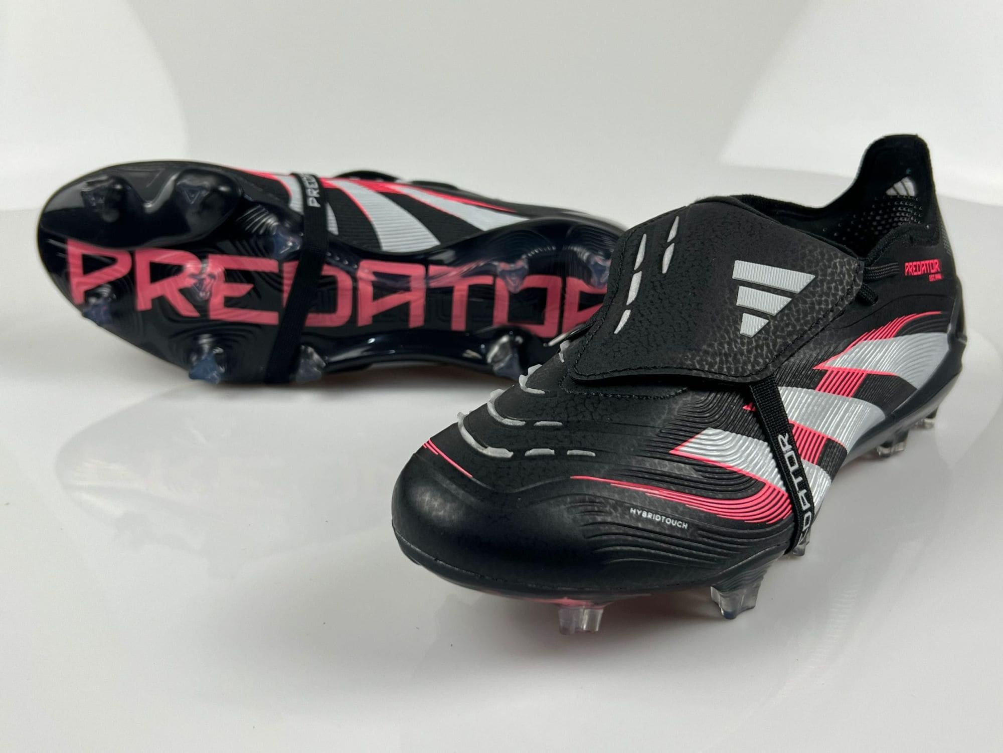 def1c2d3 | UAE SPORT STORE Pair of black and pink Adidas Predator soccer cleats with silver accents, shown on a white surface, highlighting studded soles and side branding.