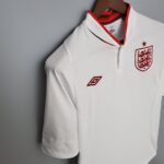 df666069_5aeee040-36f7-4e40-ad04-0be99a6d03ca | UAE SPORT STORE White England football jersey on a hanger with red trim and crest featuring three lions on the chest area