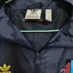 dfa04b36eb5f6126 | UAE SPORT STORE Navy Adidas jacket with visible gold trefoil logo on left chest and zipper closure, hanging on a hanger inside.