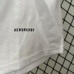 Close-up of white fabric with stitched seams and the word AEROREADY visible, set against a dark, tiled background grid.