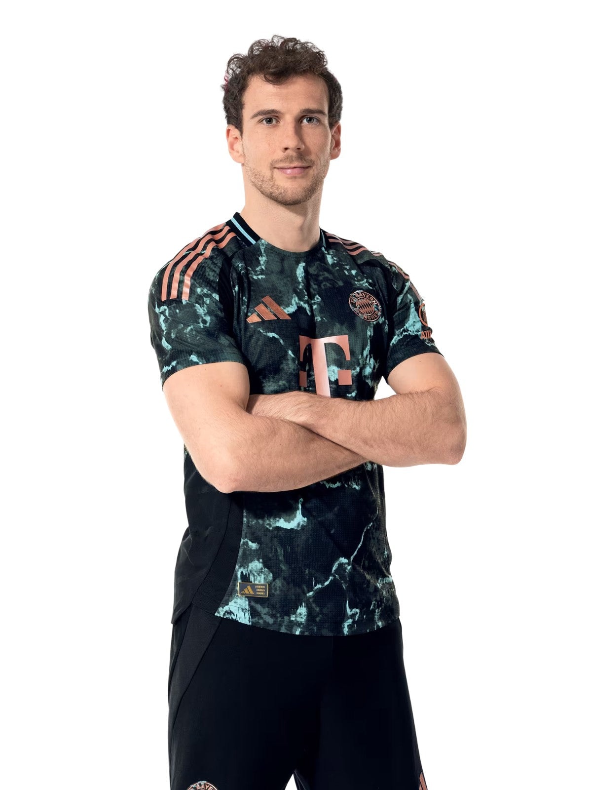 dnctZCshAv2n3PW | UAE SPORT STORE Portrait of a man with arms crossed, wearing a dark camouflage Bayern Munich football jersey, against a white studio background.