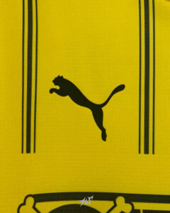 Close-up of a yellow sports jersey with a black Puma logo and two vertical black stripes on either side.