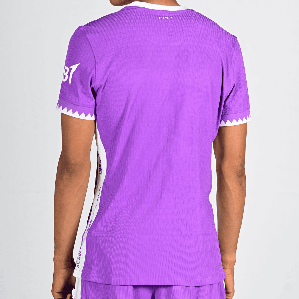 Back view of a person wearing a purple jersey, white zigzag trim on the sleeve cuffs and a white side stripe visible down the side.