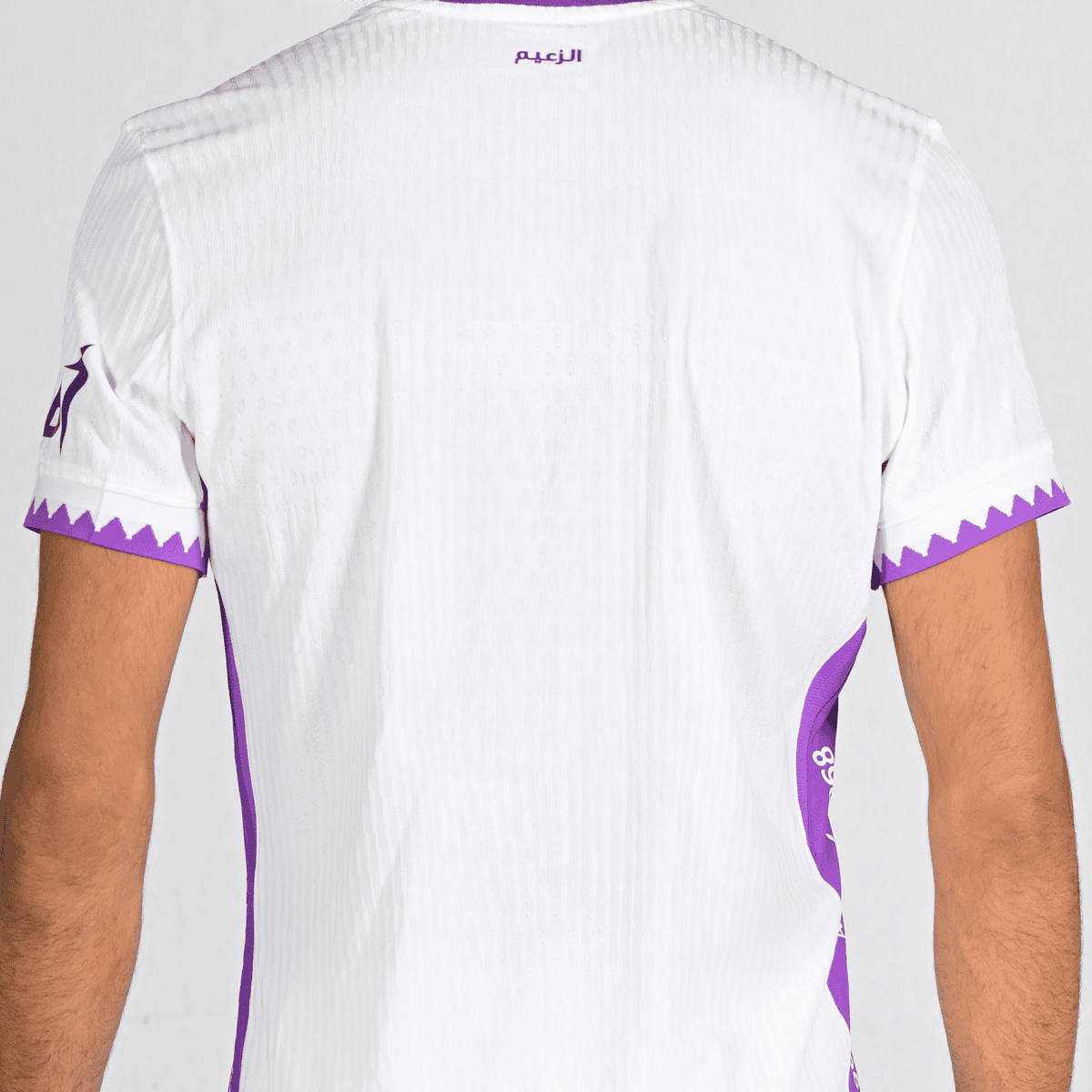 Back view of a white athletic jersey with purple trim and a purple zigzag pattern on the sleeves near the cuffs.