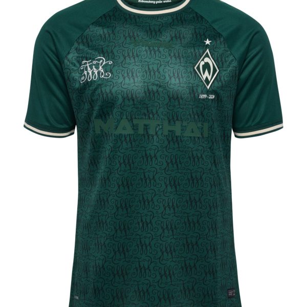 Green soccer jersey with dark teal pattern and green raglan sleeves, white‑trim collar and cuffs, club crest on the left chest and large front text/logo across the torso.