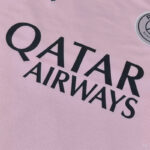 Close-up of a pink jersey featuring the black 'QATAR AIRWAYS' logo text, with a circular team patch partially visible on the right.