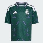 Green Saudi national team soccer jersey with geometric pattern, white Adidas logo, SAFF crest on the chest, purple accents, and white shoulder stripes.