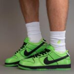 Neon green Nike sneakers with black swooshes on white socks, worn by a person standing on a neutral surface.
