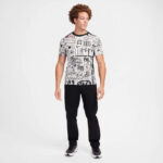 Young man in a graphic white T-shirt with black text and black joggers posing in a studio setting.