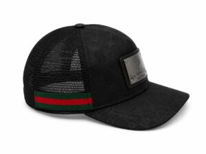 Black Gucci trucker hat with a metal plaque on the front, mesh back, and green-red-green strap at the rear.