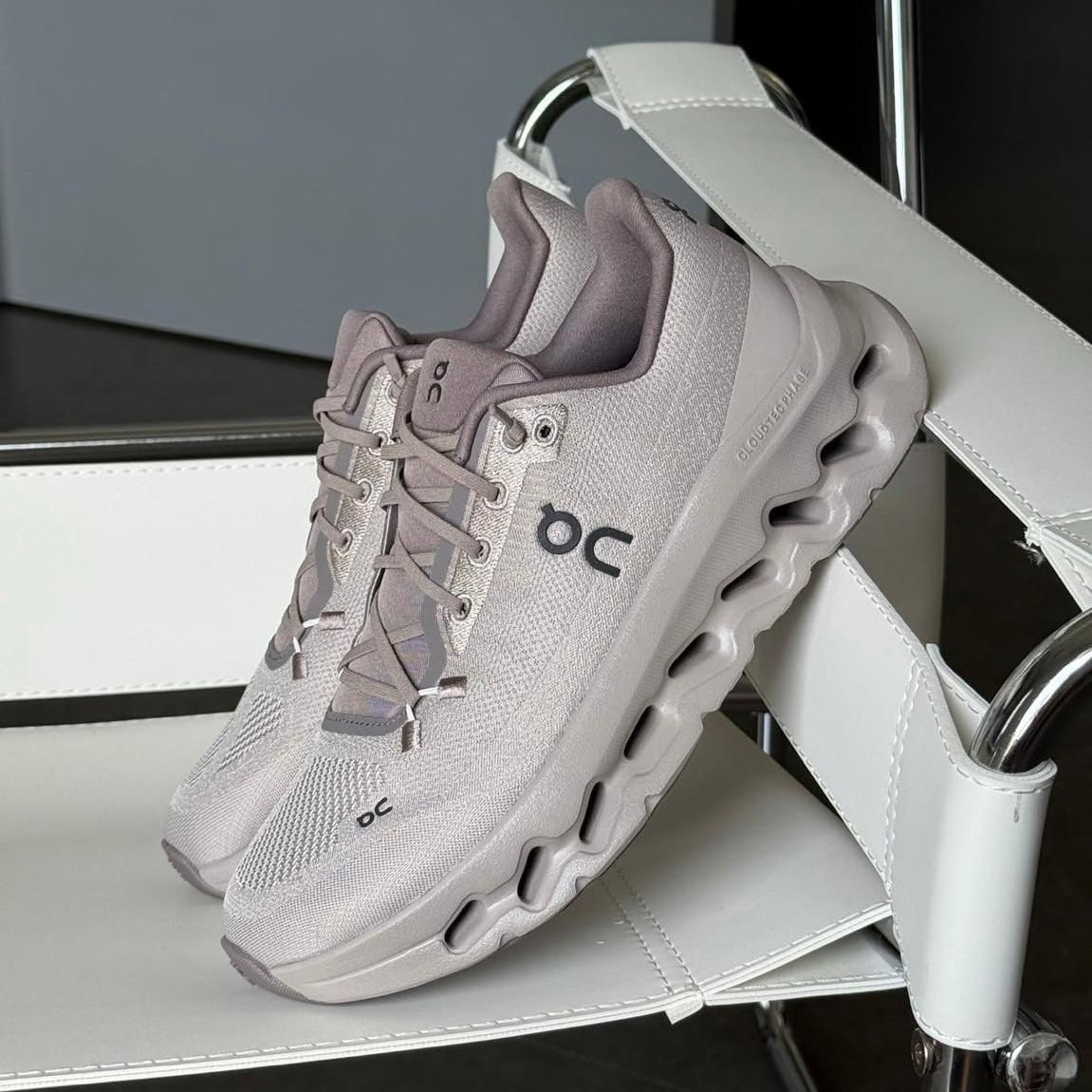 e2145d25-c4c5-4545-b518-c865adcd5031 | UAE SPORT STORE Light gray On running sneaker with a cloud-like sole resting on a white display stand in a showroom setting.