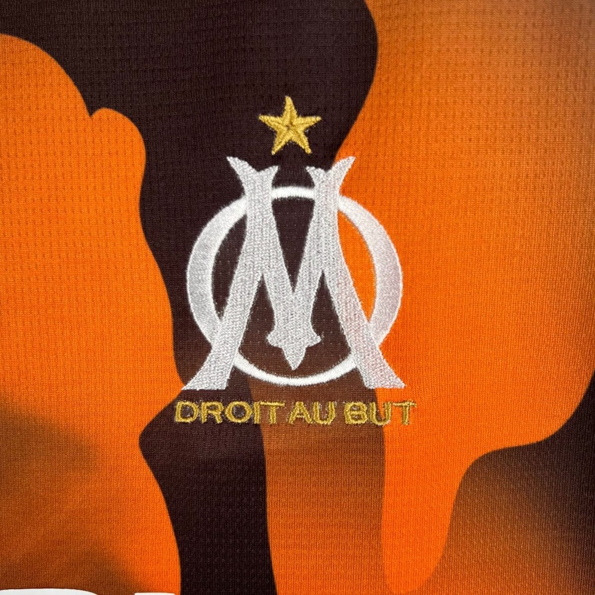Close-up of orange and brown camouflage fabric with a partial white emblem and a small gold star.