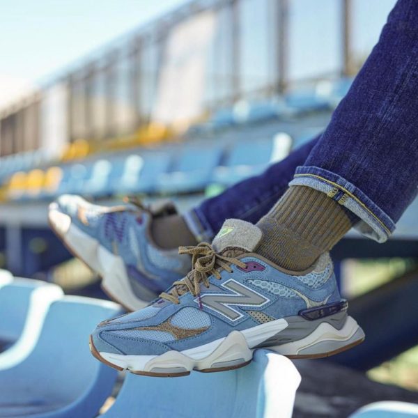 Blue and gray athletic sneakers resting on light blue stadium seats, with jeans cuffs and brown socks visible.