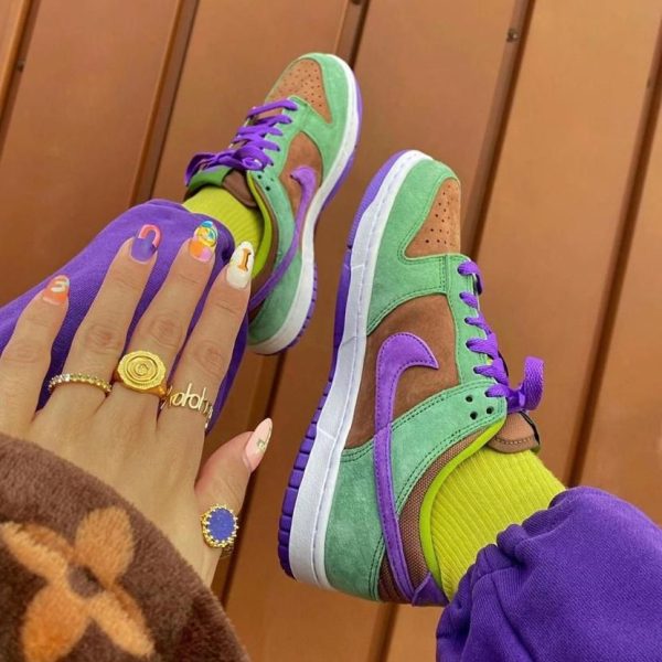 Colorful sneakers in green, purple, and brown with purple laces, worn with bright yellow socks and purple pants.