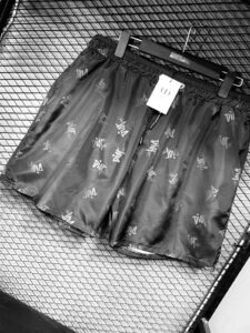 Black shorts with repeated 'Dior' logo, hanging on a clothes hanger against a mesh background.