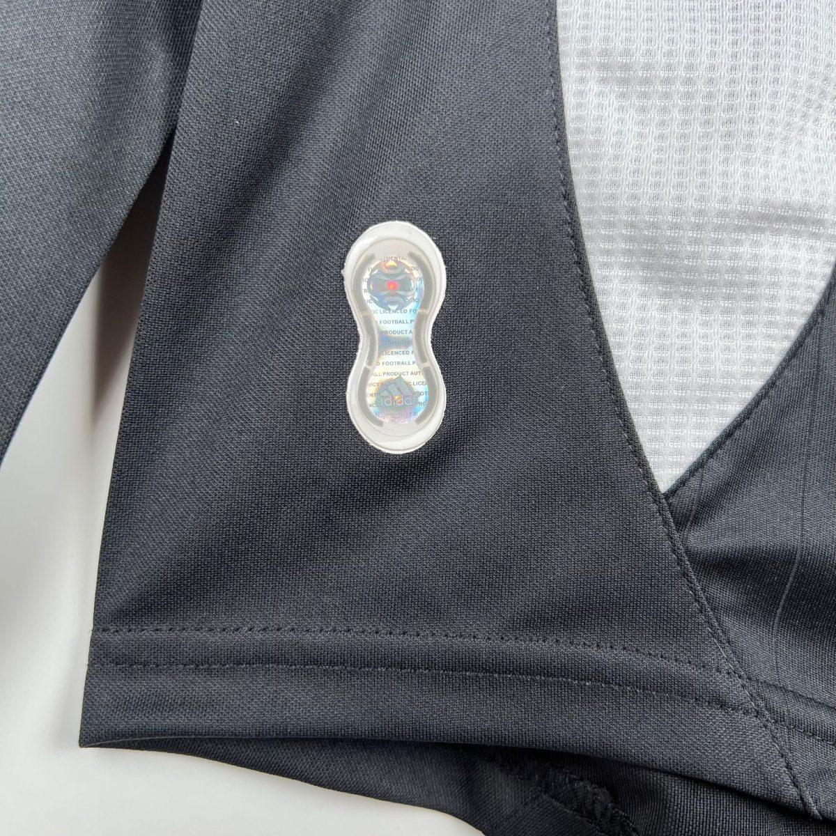 Close-up of a dark textured blazer lapel with a small clear security tag attached to the fabric at the center.