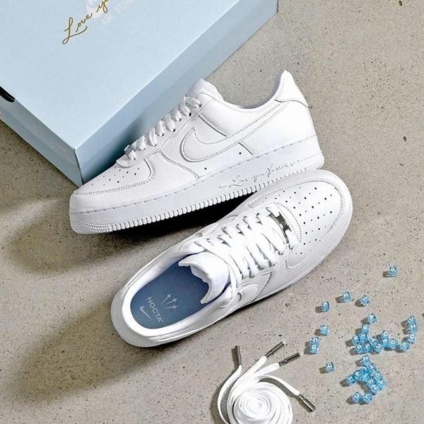 White Nike sneakers with matching white laces, a light blue box reading 'Love you forever', and spare laces on a concrete floor.