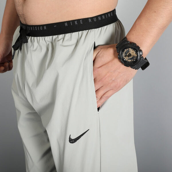 Close-up of a person wearing light gray Nike running shorts with a black waistband, hand in the side pocket, and a black sport watch visible on the wrist.