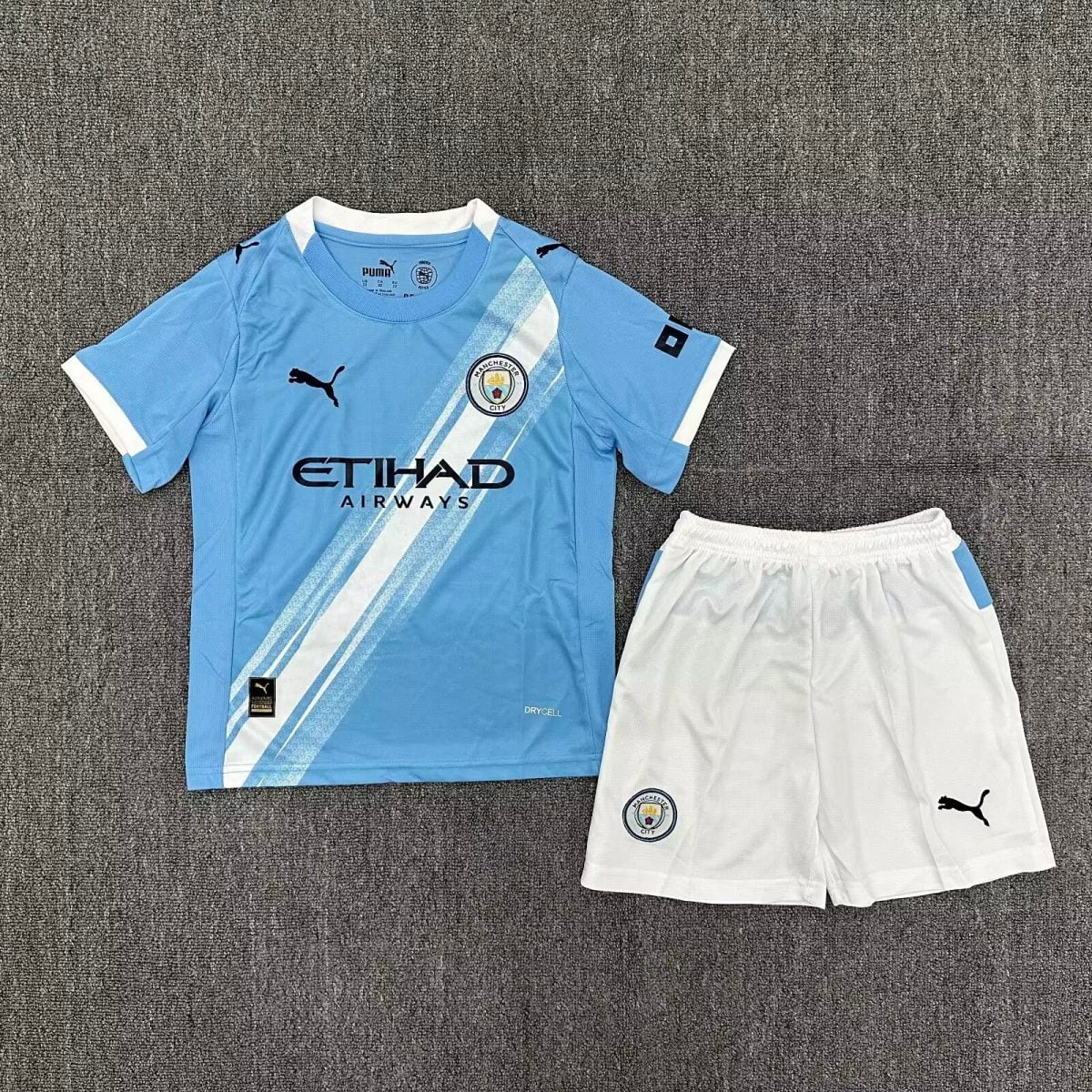Manchester City football kit laid flat: light blue jersey with diagonal white stripes, club crest, and Etihad Airways sponsor, paired with white shorts and Puma logos.