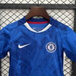 Blue Chelsea FC football jersey on a wooden hanger, crest visible on the chest against a metal grid background.
