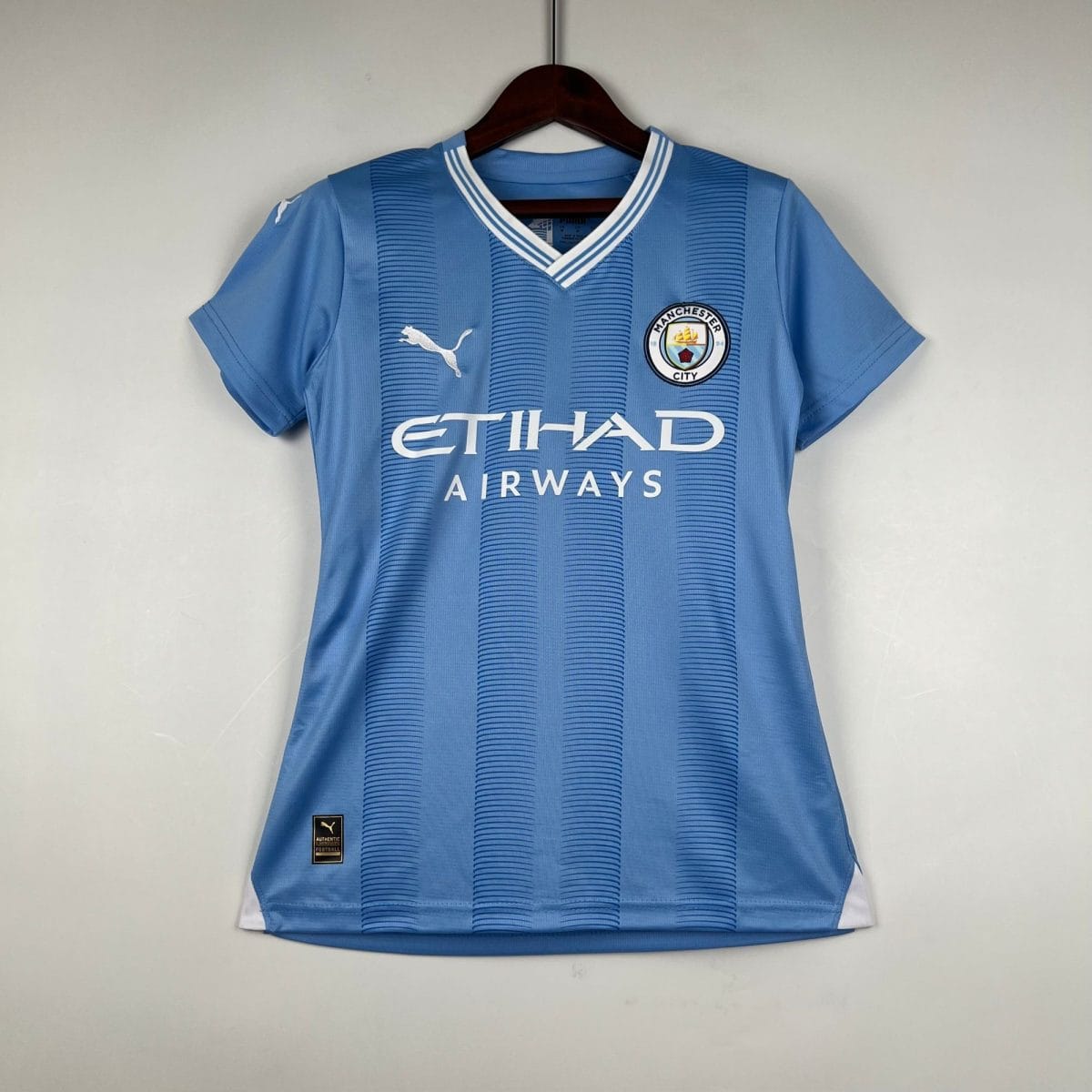 Blue Manchester City football jersey on a hanger, featuring the club crest and Etihad Airways sponsor text.