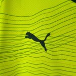 Close-up of neon yellow fabric with dark wavy lines running diagonally and a black irregular blot in the lower center.