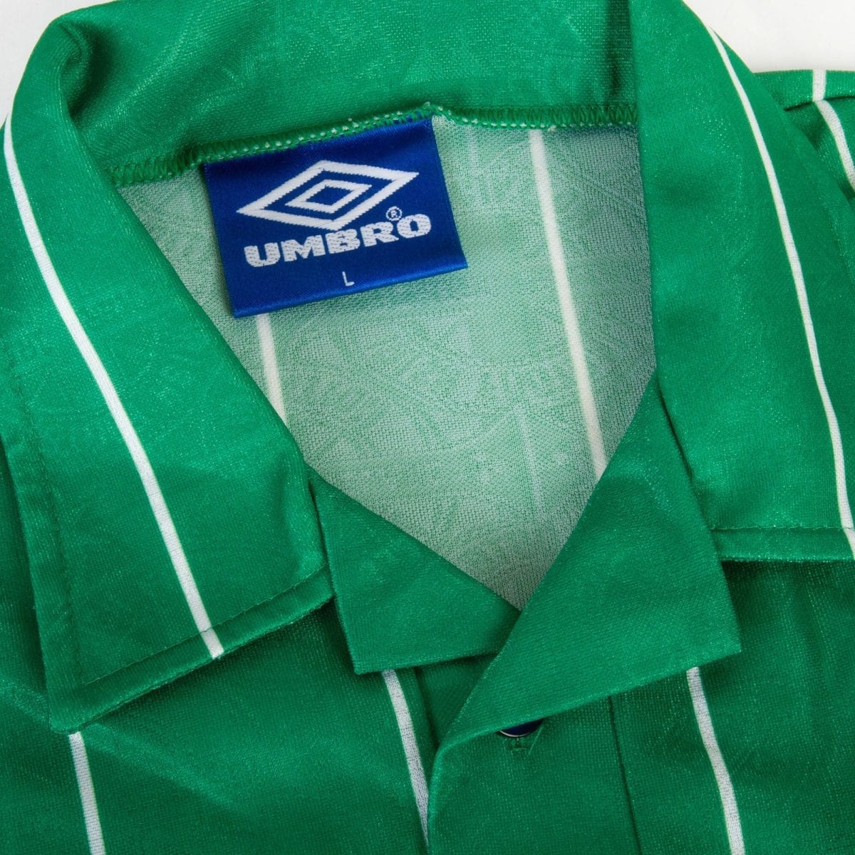 Close-up of a green fabric jacket with a blue Umbro brand tag reading size L nearby the seam.