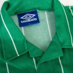 Close-up of a green fabric jacket with a blue Umbro brand tag reading size L nearby the seam.