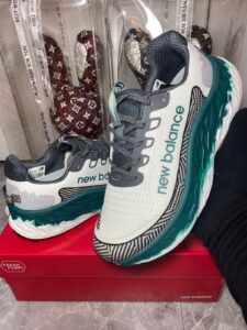 White and teal New Balance Fresh Foam running shoes resting on a red box, showing logo text and teal sole details.