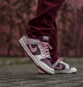 e5242f6c-3ede-404a-ba3a-908fd0bca390 | UAE SPORT STORE Low-angle shot of burgundy and pink Nike sneakers mid-step on a pavement, worn with maroon pants.