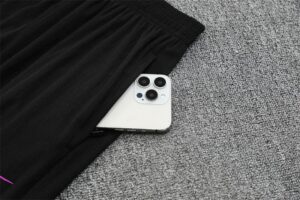 White iPhone with triple-camera bump poking out from under a black garment on a gray carpet floor.